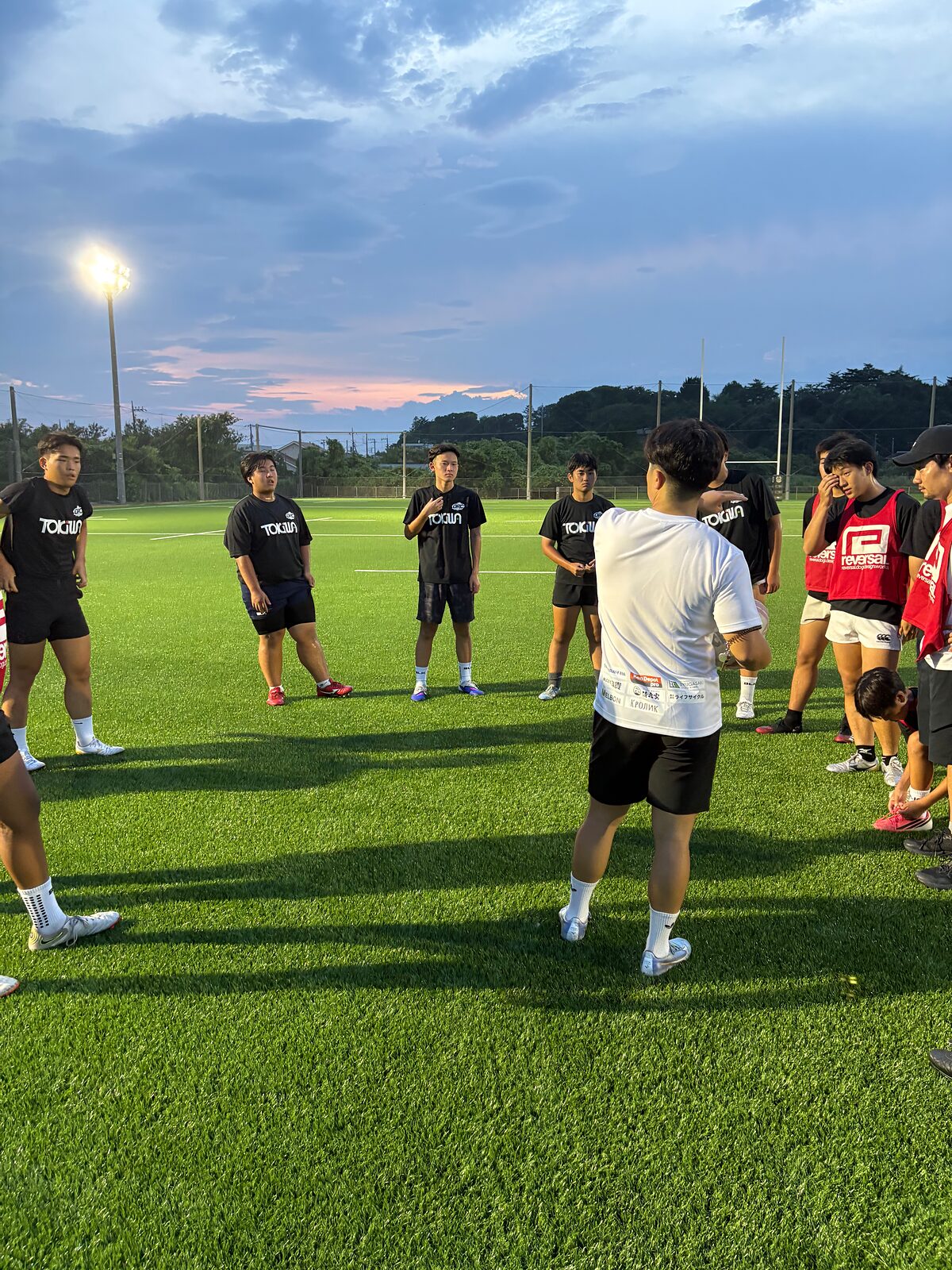 夕暮れのグラウンドで輪になって話す選手たち